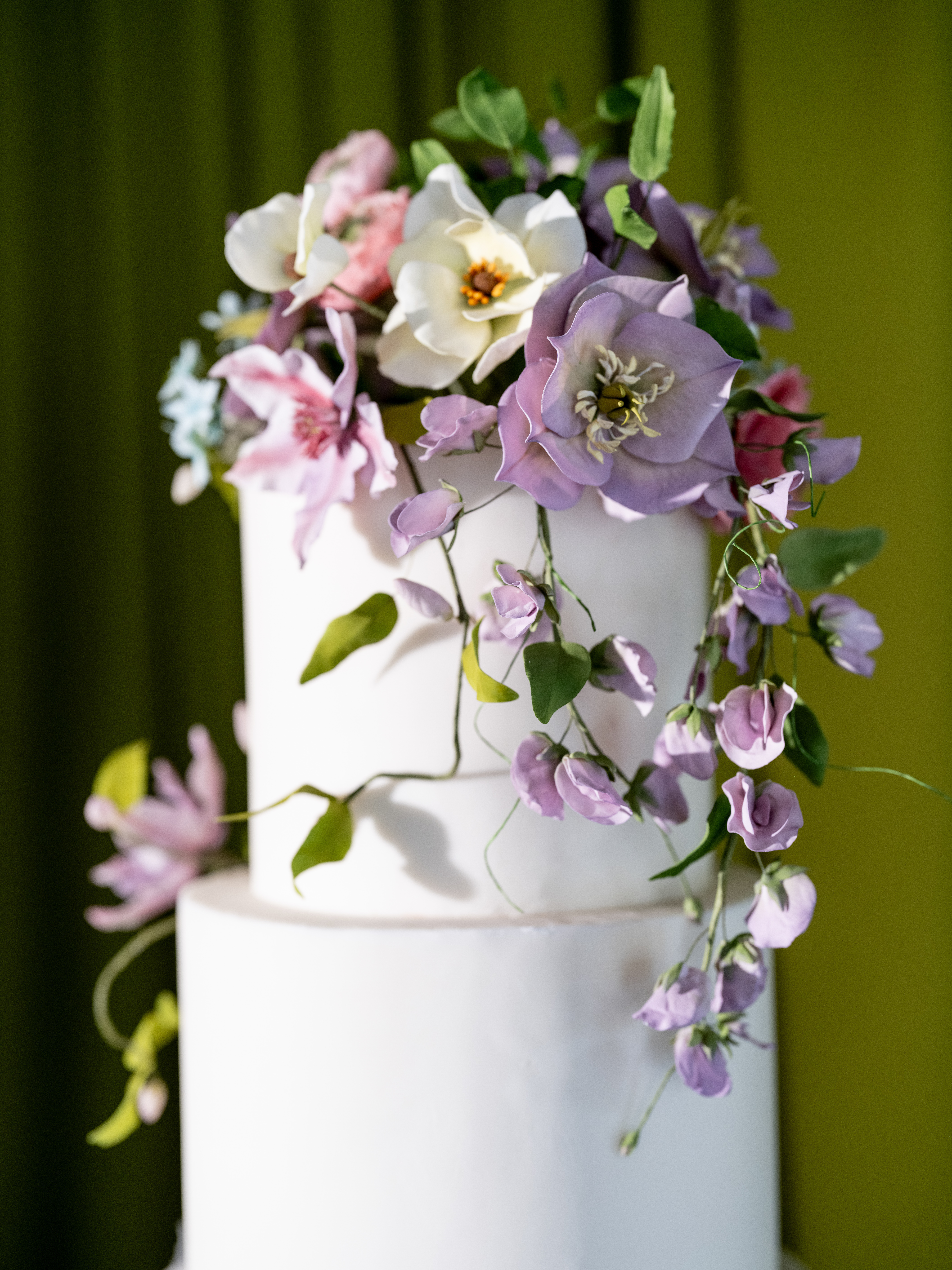 Close-up detail of a white wedding cake topped with ivory magnolias, lavender anemones, and trailing sweet pea sugar flowers